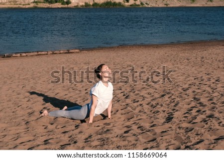 Woman stretching yoga on the beach by the river in the city. Beautiful view. Urdhva Mukha Shvanasana pose.
