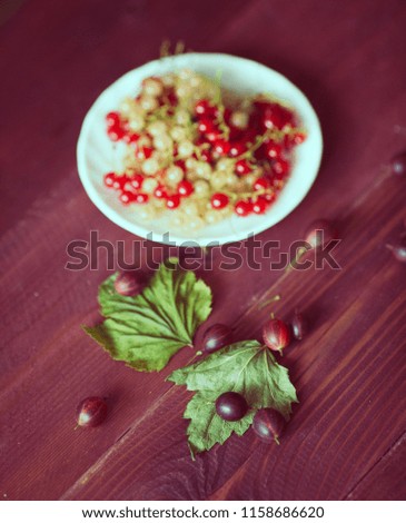 Berries of a currant, gooseberries on a saucer, leaves, on a natural wooden background