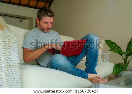 young attractive and handsome happy man sitting at home sofa couch working with laptop computer netbook relaxed smiling focused in internet business success and online freelance job concept
