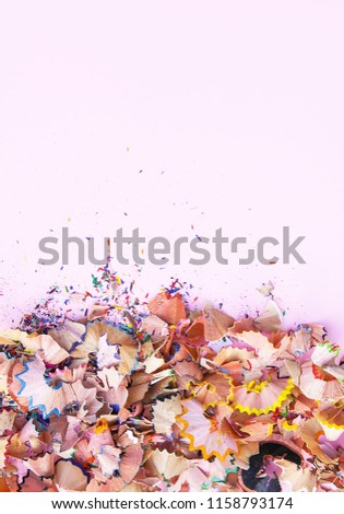 Wooden pencil shavings and colorful crumbs of graphite from sharpener on soft pink pastel paper background. Top view. Design elements for poster, banner, cards. Creative design.
