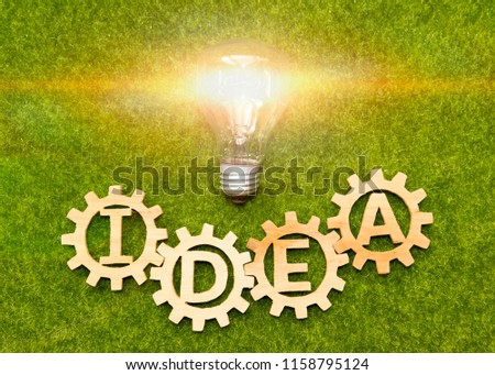 word idea, gears made of wood, electric bulb on the background of artificial grass of green color. concept of a fresh business idea.