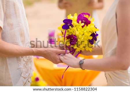 Bride and groom getting married on a colorful tropical beach wedding. Purple and yellow flower bouquet.