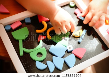 A child plays with colorful pieces of a puzzle on a black board