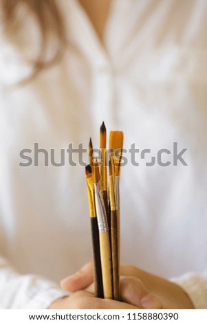 Young caucasian woman artist painter in white shirt hold in hand bunch of different types of paint brushes. Arts creativity painting concept. Poster banner with copy space