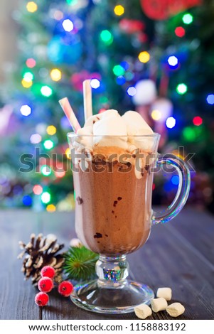 Glass cup of hot cocoa with mini marshmallows with pine boughs a rustic background with beautiful Christmas lights of bokeh. Could also be coffee.