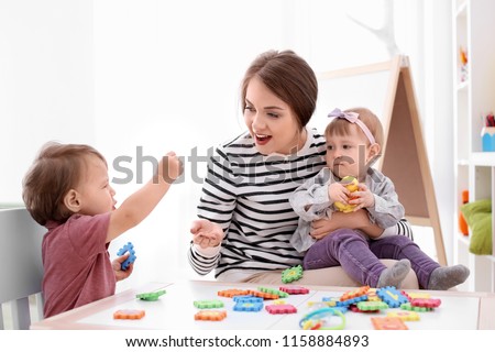 Young nanny playing with cute little children at table, indoors Royalty-Free Stock Photo #1158884893