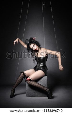 Woman posing as a marionette puppet in black and red with transparent strings. Conceptual fine art about manipulation and control.
