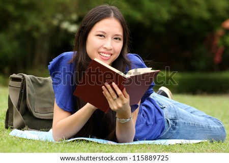 Pretty young woman reading a book at park with smile