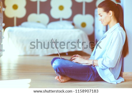 Young woman sitting on the floor near children's cot with laptop. Young mom