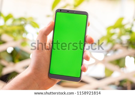 Holding a smartphone on hand with a blank green screen