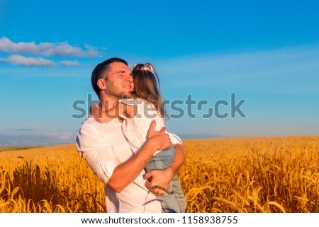 Happy family - father holding daughter in his arms in the middle of a wheat field against a blue summer sky