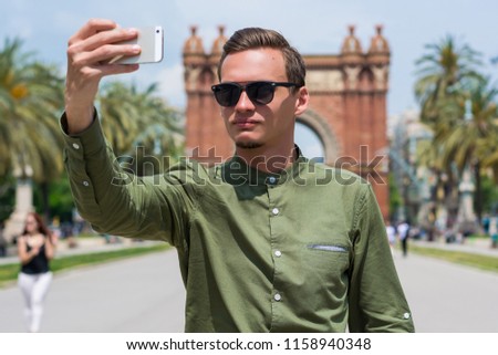 A young guy, a tourist in glasses, makes selfie  near the Arc de Triomf  in the city of Barcelona in Catalonia, Spain