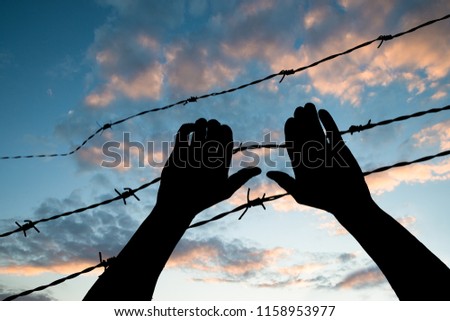 Low Section View Of A Refugee Hand Holding Barbed Wire Fence