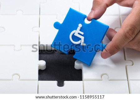 Human hand solving jigsaw puzzle with blue piece having handicap icon