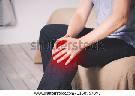 Man with pain in knee suffering at home, painful area highlighted in red