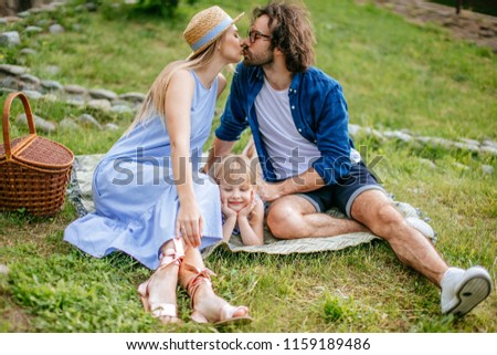 happy family man woman and little girl playing outside. Young family having fun picnic together. parents kissing