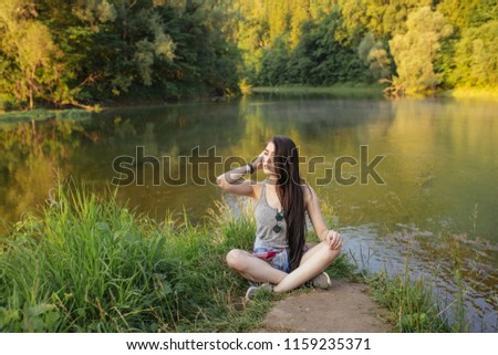 Portrait of pretty pensive woman sitting on the green grass with awesome landscape on the background of the photo. beauty and youth concept