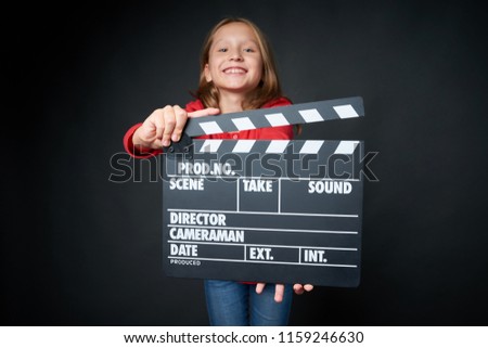 Happy smiling girl holding clap board, over dark background. Shallow depth of field, focus on clapper board
