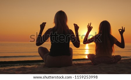 Mom and daughter are meditating by the sea at sunset. Health and happy time together