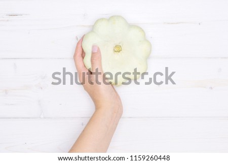 One whole summer white pattypan squash in a woman hand flatlay on grey wood