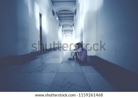Picture of Asian schoolgirl looks depressed while sitting alone in the school corridor