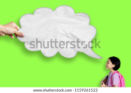 Picture of cute schoolgirl carrying a book while looking at an empty cloud bubble. Shot with green screen