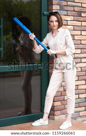 the girl stands at the closed door of the store and tries to break it with a baseball bat