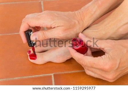 Hands paint toenails red on stone floor