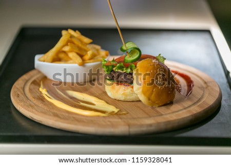Tasty beef burger with fresh fries. Concept of fast food. Grilled beef burger with lettuce and mayonnaise served on pieces of brown paper on rustic wooden table. An american burger with fried potatoes