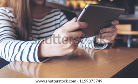 Closeup image of an asian woman holding , looking and using tablet pc in modern cafe