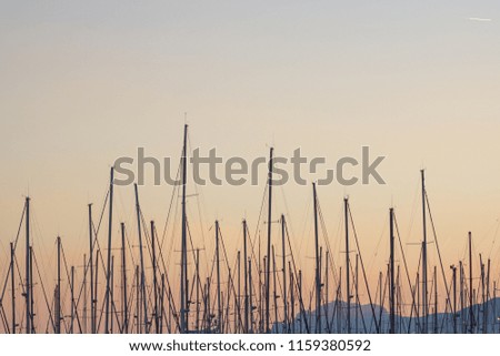 Low angle view over several boat masts in the beautiful orange sunset sky, with moutains in background, Cannes harbour, French Riviera, France.