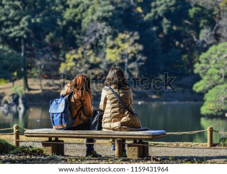 Young woman sitting on wooden bench at city park in sunny day.