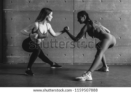 Fit woman wrestle on hands with a female opponent looking in her eyes.