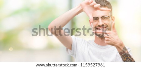 Young tattooed adult man smiling making frame with hands and fingers with happy face. Creativity and photography concept.
