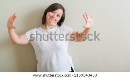 Down syndrome woman standing over wall showing and pointing up with fingers number ten while smiling confident and happy.