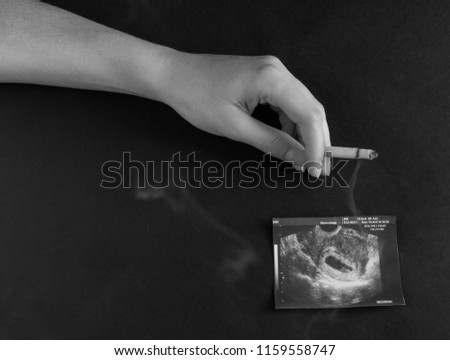 A woman's hand holds a burning cigarette against the background of a picture of the uzi of pregnancy, pregnancy and smoking, gestation