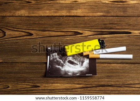 Cigarette and lighter lay on the picture of uzi pregnancy, smoking and pregnancy, gestation, wooden background