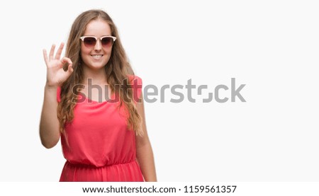 Young blonde woman wearing pink sunglasses doing ok sign with fingers, excellent symbol