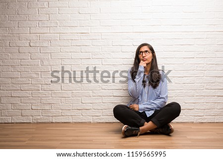 Young indian woman sit against a brick wall doubting and confused, thinking of an idea or worried about something Royalty-Free Stock Photo #1159565995