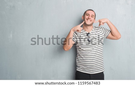 Young caucasian man over grey grunge wall smiling confident showing and pointing with fingers teeth and mouth. Health concept.