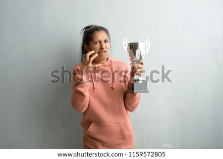 Young sporty indian woman against a wall very angry and upset, very tense, screaming furious, negative and crazy. Holding a trophy.