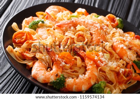 Pasta fettuccine with squid, tiger shrimps, vegetables, parmesan cheese and tomato sauce close-up on a plate on a table. Horizontal
