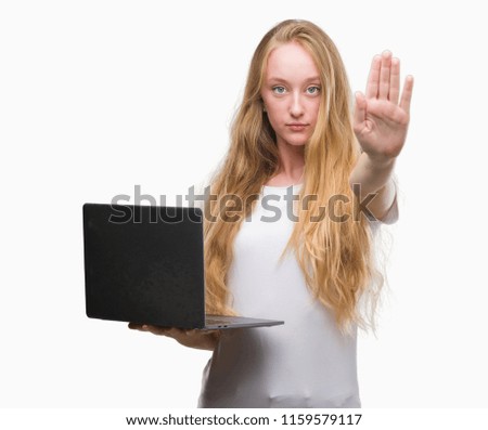 Blonde teenager woman using computer laptop with open hand doing stop sign with serious and confident expression, defense gesture