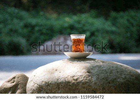 Eastern black tea in glass on a stone at forest. Eastern tea concept. Armudu traditional cup. Green nature background. Selective focus