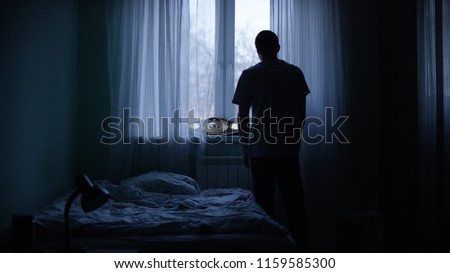 Alone man silhouette staring at the window closed with curtains in bedroom. Man stands at window alone Royalty-Free Stock Photo #1159585300