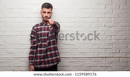 Young adult man over white brick wall pointing with finger to the camera and to you, hand sign, positive and confident gesture from the front