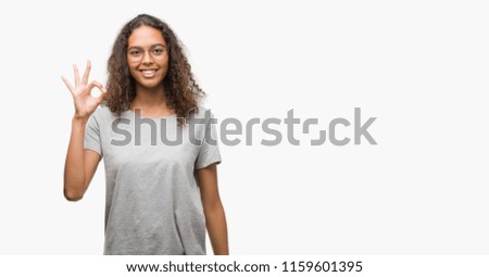 Beautiful young hispanic woman wearing glasses smiling positive doing ok sign with hand and fingers. Successful expression.