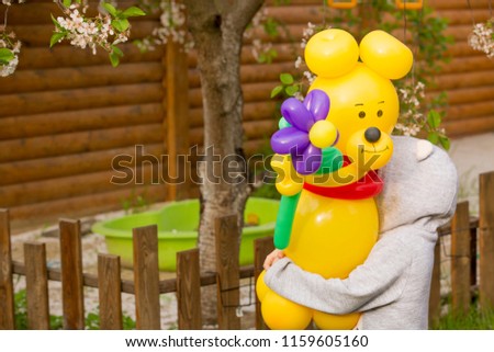 little girl holding large yellow bear from balloons with a big flower in the garden, Congratulations on the occasion