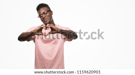 Young african american man wearing pink t-shirt smiling in love showing heart symbol and shape with hands. Romantic concept.