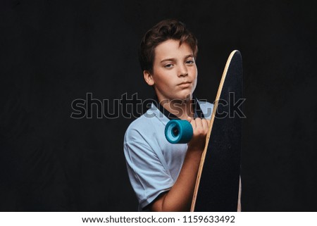 Portrait of a young skater boy dressed in a white t-shirt holds a longboard. Isolated on the dark background.